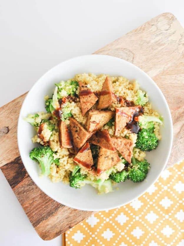 BBQ couscous bowl with pan fried tofu triangles and broccoli florets in a white bowl on a wooden board