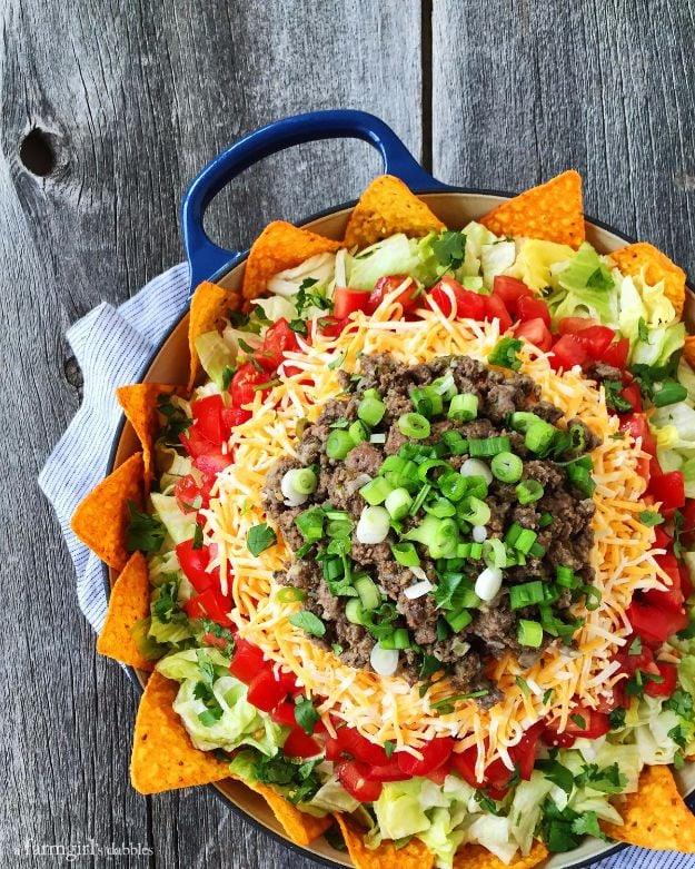 Taco salad with Doritos, seasoned beef, lettuce, tomatoes and green onions in a blue handled skillet