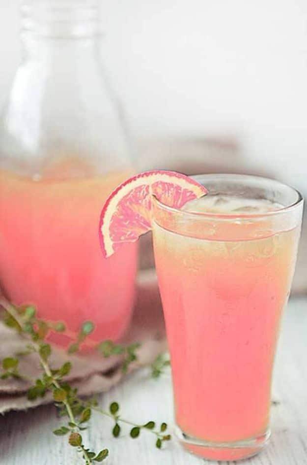 Tall glass of pink peach lemonade with a peach slice on the rim, mint leaves and a bottle pitcher behind it
