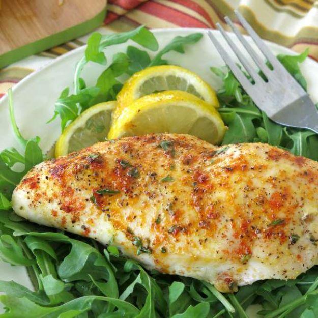 Baked lemon pepper chicken, a seasoned chicken breast on a bed of arugula with lemon slices and a fork
