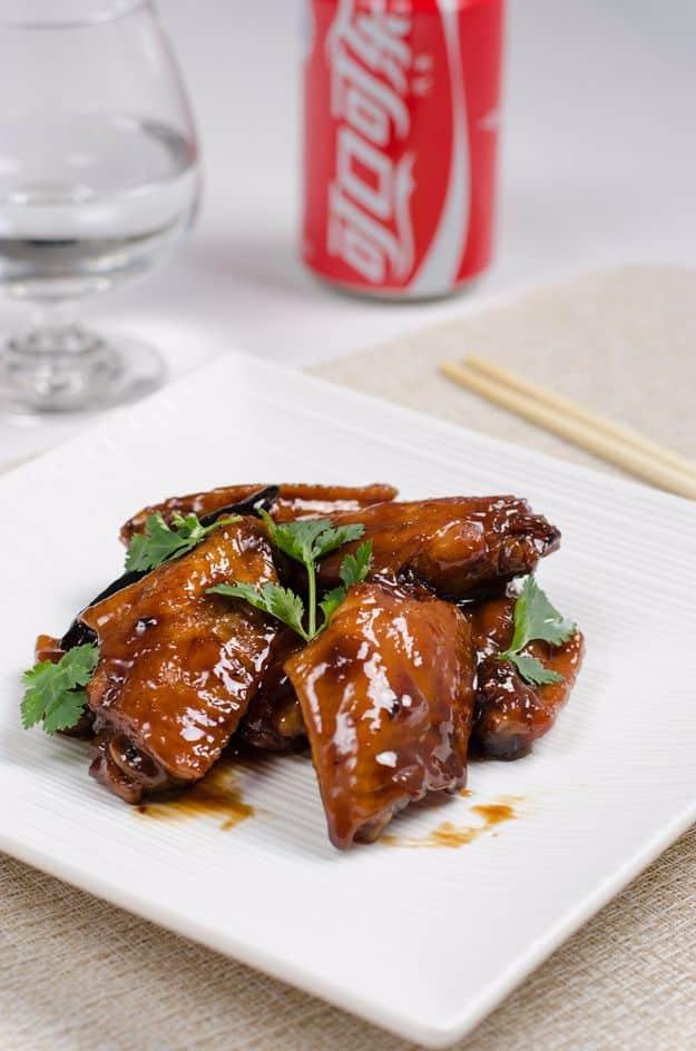 Braised Coca-Cola chicken wings, three deep mahogany glazed wings on a square white plate with cilantro and chopsticks