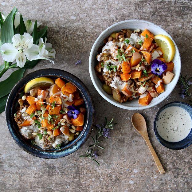 Two bowls of harissa lentils with roast squash, tahini dressing and pine nuts styled with flowers and a spoon