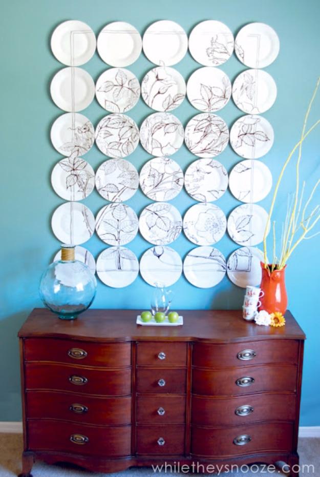 Grid of thirty white plates on a turquoise wall, hand drawn with brown botanical sketches above a wooden dresser