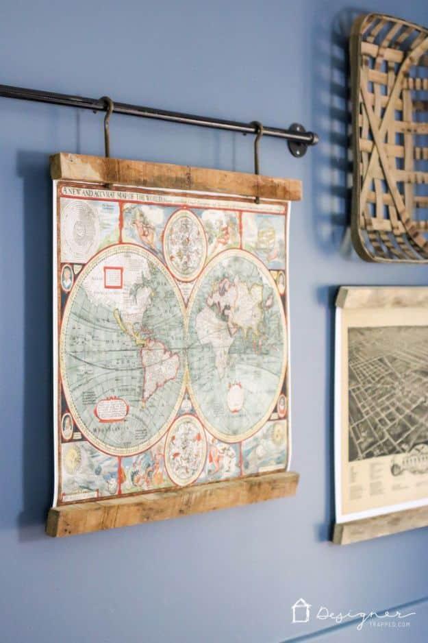 Framed antique world map in a reclaimed wood frame hanging from an iron pipe rail on a blue wall beside a tobacco basket