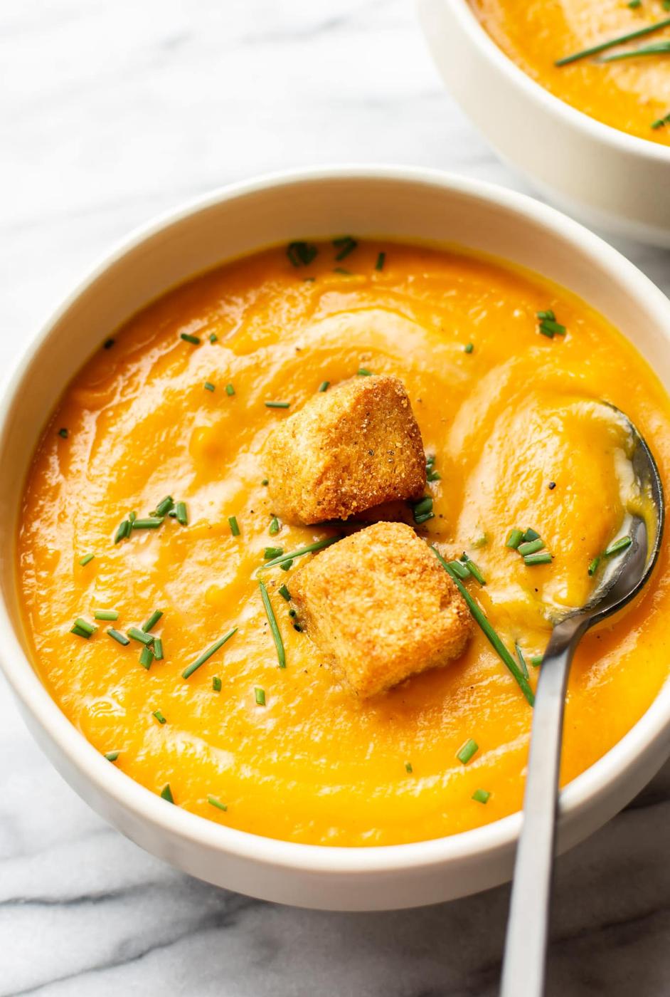 Roasted fall vegetable soup in a bowl, thick orange puree swirled with cream and scattered with croutons