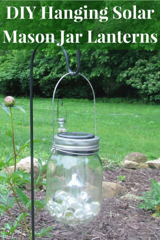 DIY hanging solar mason jar lanterns graphic with a pebble filled jar on a shepherd's hook in a garden