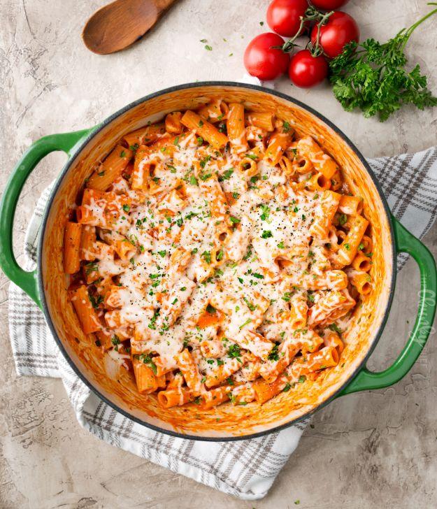 One pot chicken parmesan pasta in a green Dutch oven, melted cheese over red sauce pasta with chopped parsley