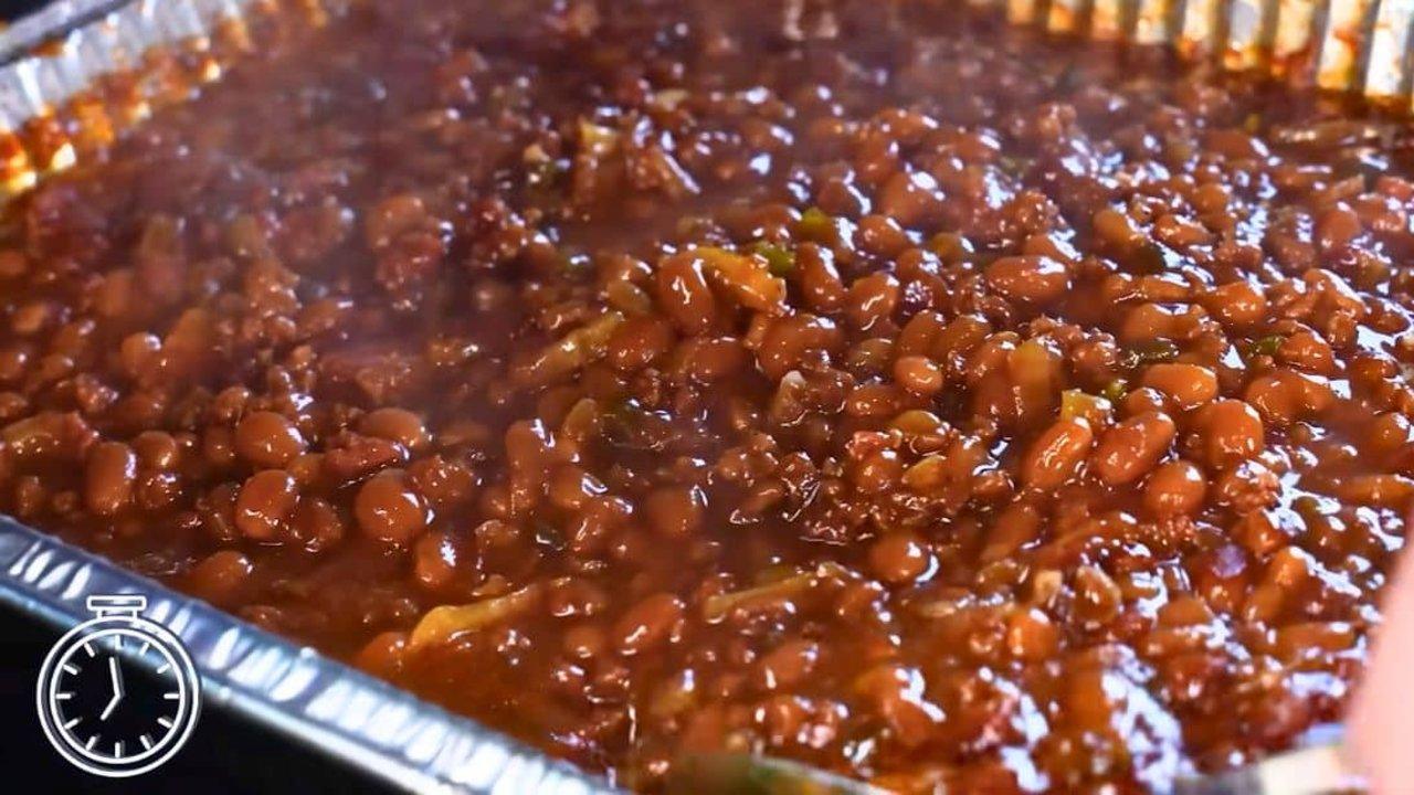 Pit style BBQ baked beans loaded with ground beef, bacon and bell pepper in a cast iron pan at a cookout