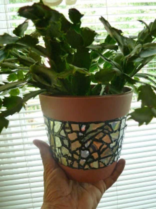 Terra cotta colored plastic flower pot with a band of CD mosaic pieces and black grout lines, held in a hand