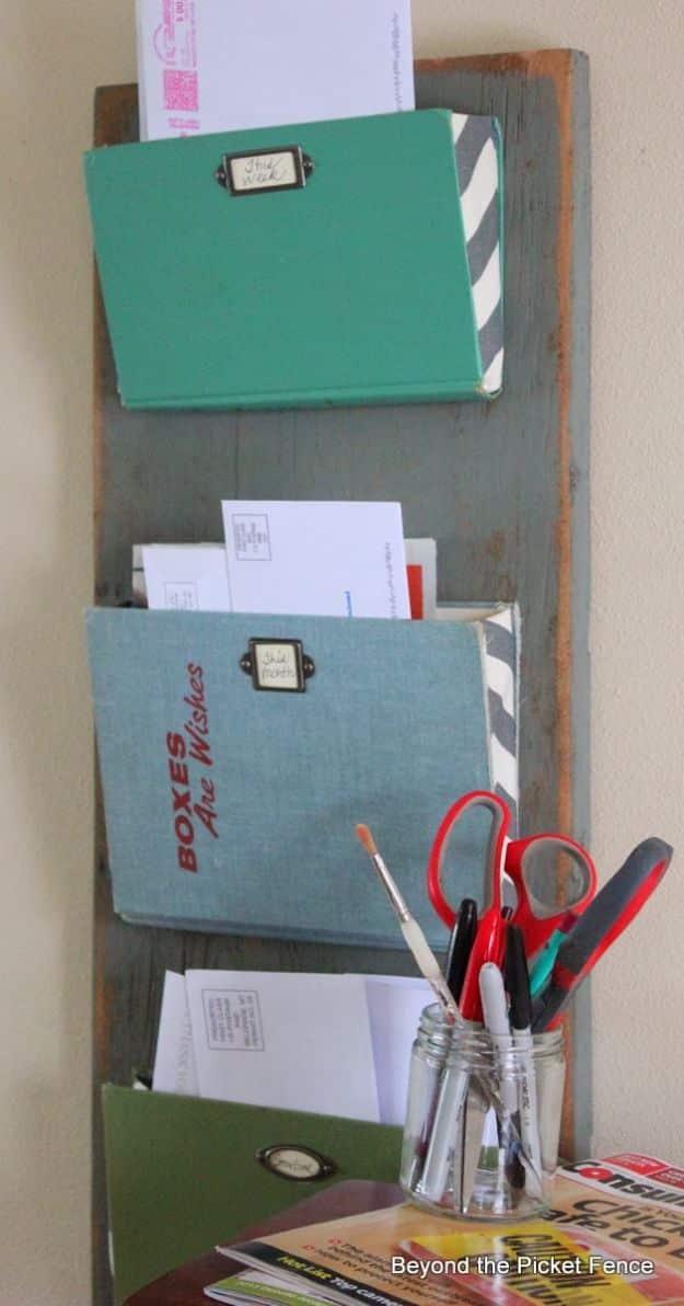 Three vintage hardback book covers screwed at an angle to a gray barn wood board as mail pockets with metal label holders