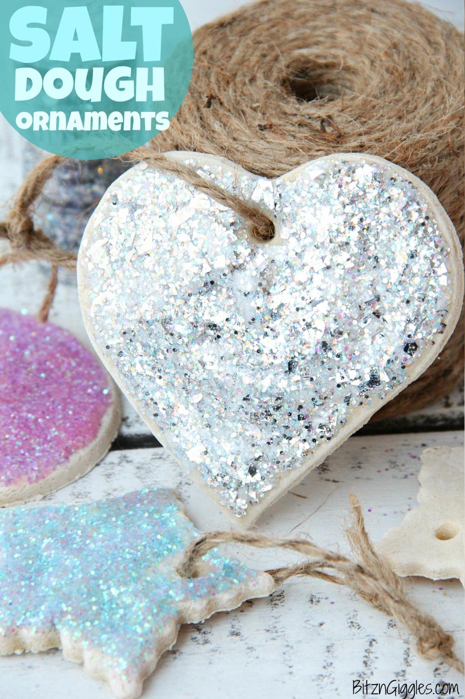 A silver glitter salt dough heart ornament on jute twine with pink and blue glittered ornaments beside a spool of twine