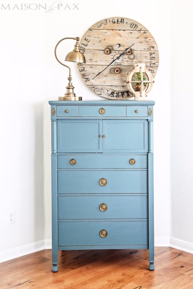 Tall vintage dresser painted deep blue with its original brass drop pulls kept, styled with a brass lamp and a wall clock