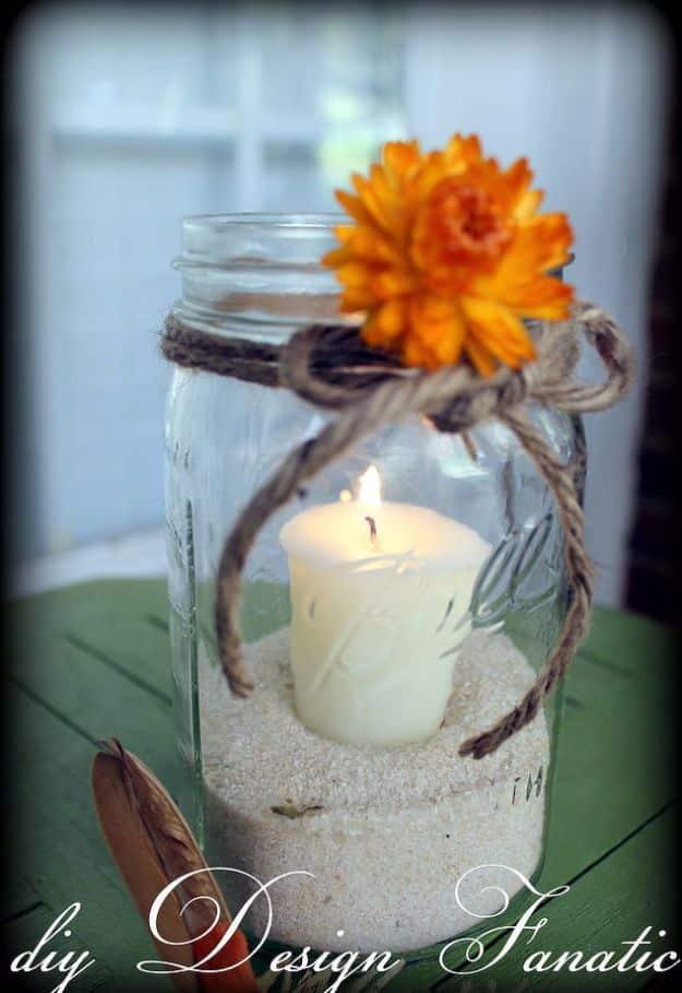 Mason jar candle holder wrapped in twine with a dried orange flower, holding a lit white pillar candle