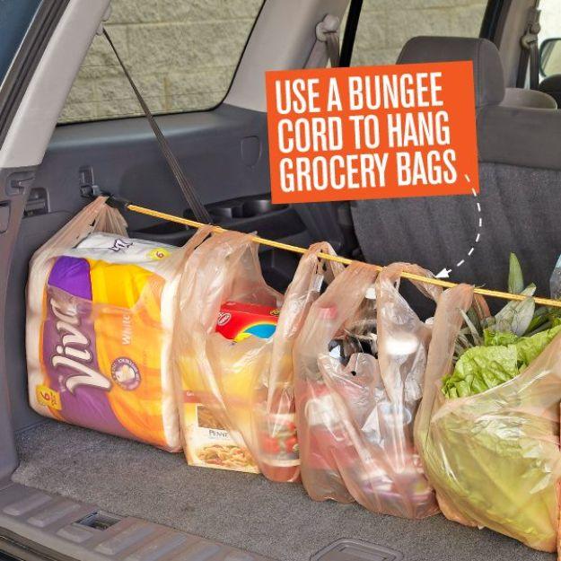 Hanging groceries in a car, five grocery bags of shopping suspended upright from a yellow bungee cord in a trunk
