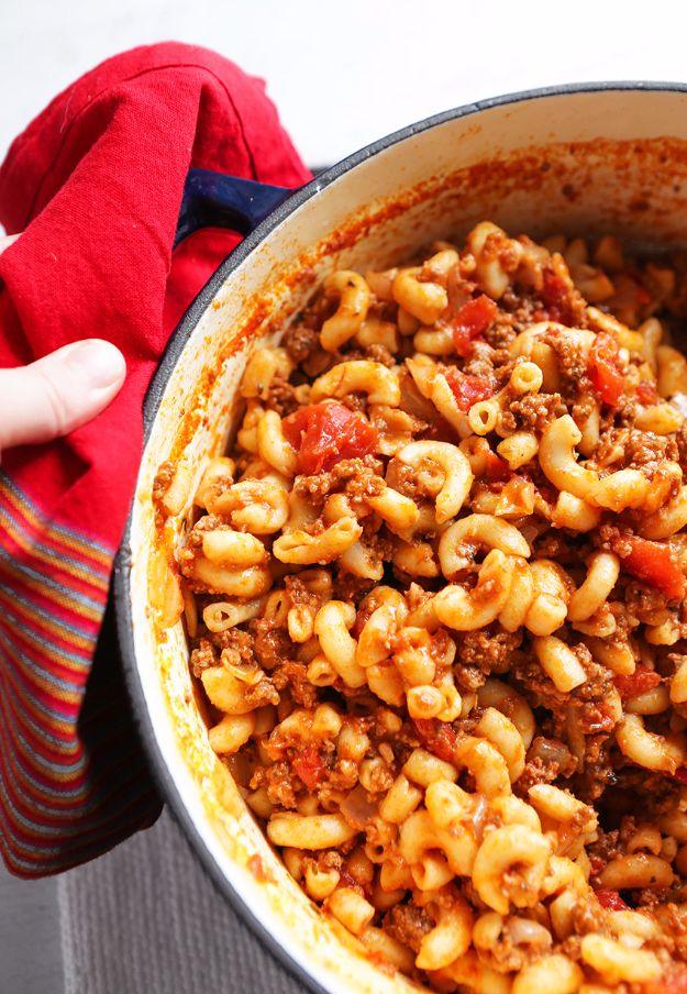 American goulash in a big white pot, elbow macaroni in tomato sauce with ground beef, held with a red oven mitt