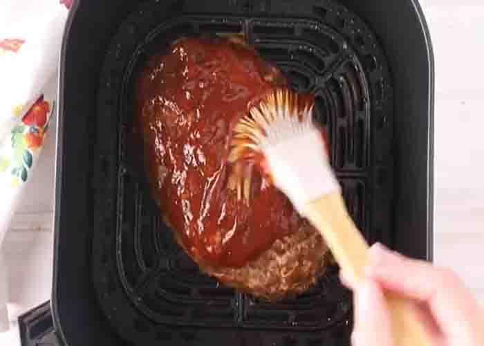 Brushing the top of the air fryer meatloaf with glaze