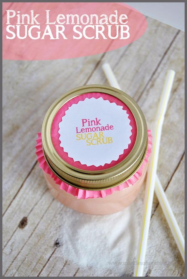 Pink lemonade sugar scrub in a jar with a gold lid and round pink label, two paper straws on grey boards
