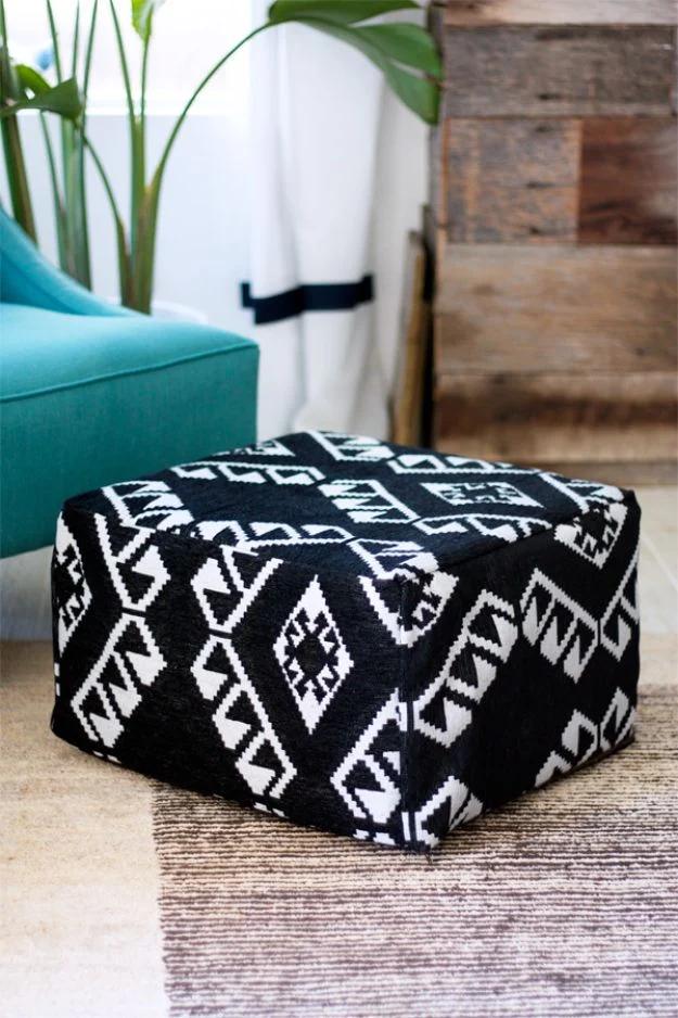 Round black and white patterned pouf ottoman on a gray rug beside a teal chair and a reclaimed wood wall