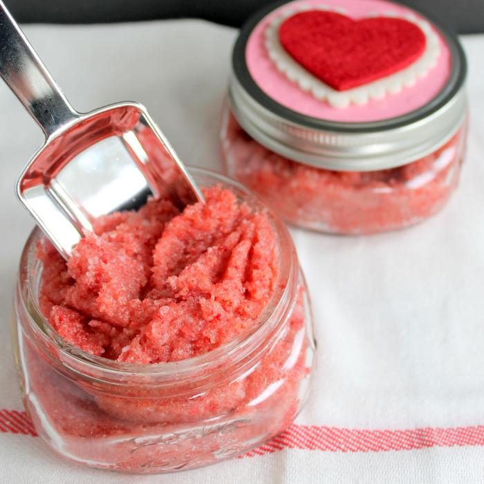 Bright pink strawberry sugar scrub in two small glass jars, one open with a metal scoop, one topped with a heart