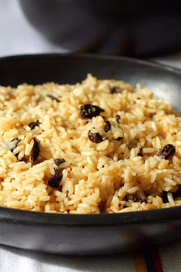 Arroz con Coca Cola, golden rice studded with dark raisins served in a black cast iron skillet on a woven mat