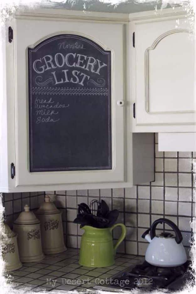 Chalkboard grocery list panel set into a cream cabinet door above olive grid tile and a green pitcher