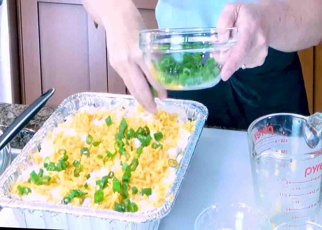 Garnishing the baked potato casserole with chopped green onions and shrrGarnishing the baked potato casserole with chopped green onions and shredded cheddar cheese