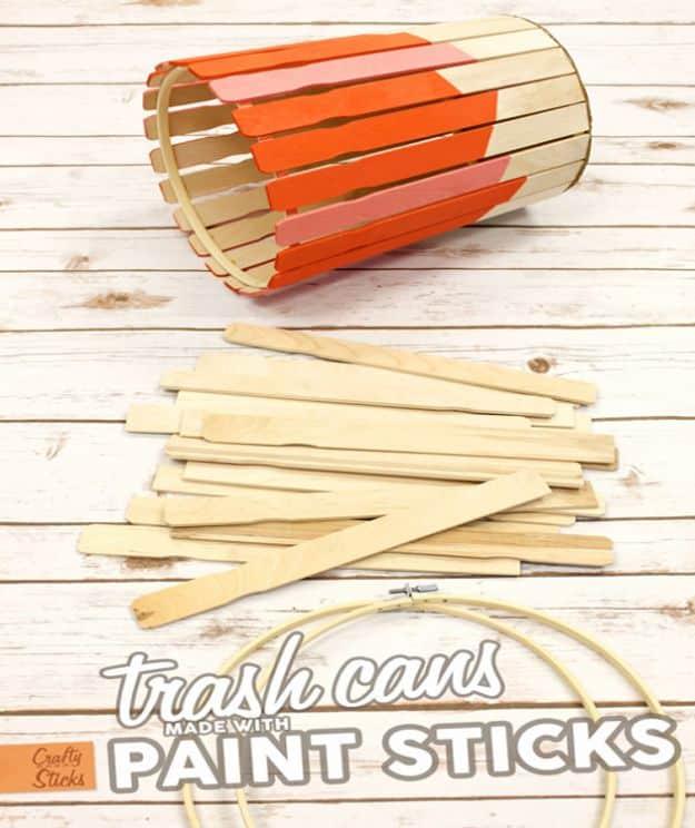 Trash can built from wood paint stir sticks dipped orange, lying beside loose sticks and an embroidery hoop