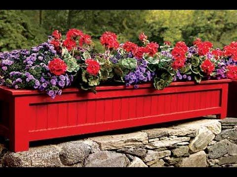 DIY curb appeal planter box painted red and filled with geraniums and petunias on a dry stone garden wall