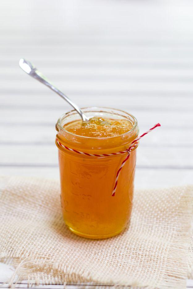 Salted cantaloupe jam in half pint canning jars, pale orange, with fresh cantaloupe slices on a cutting board