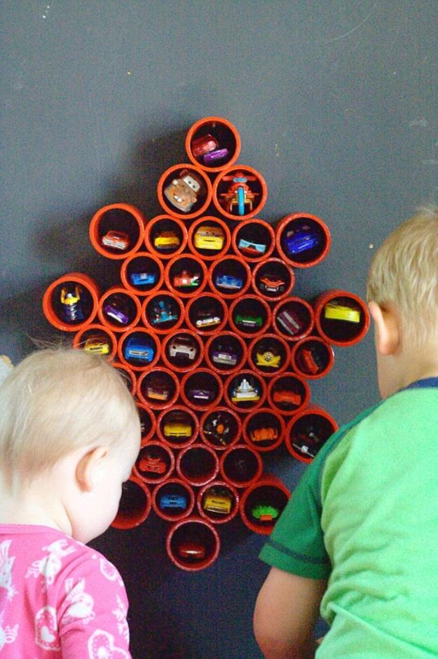 DIY matchbox car storage, two children looking at a red pyramid of PVC pipe rounds holding toy cars on a gray wall