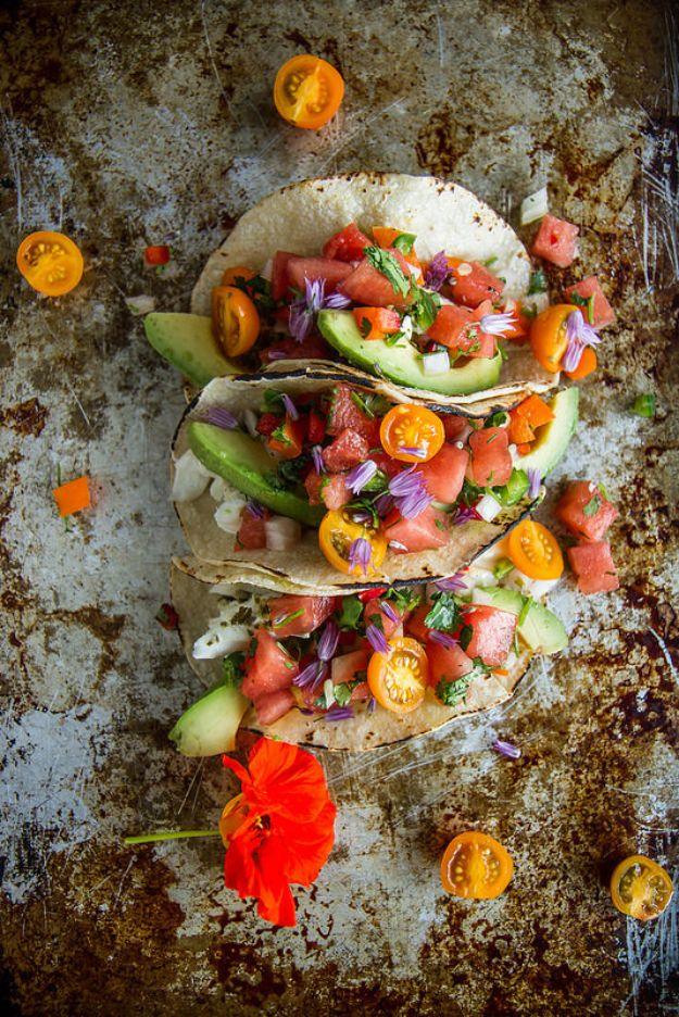 Grilled halibut tacos topped with diced watermelon salsa, avocado and edible flowers on a dark sheet pan