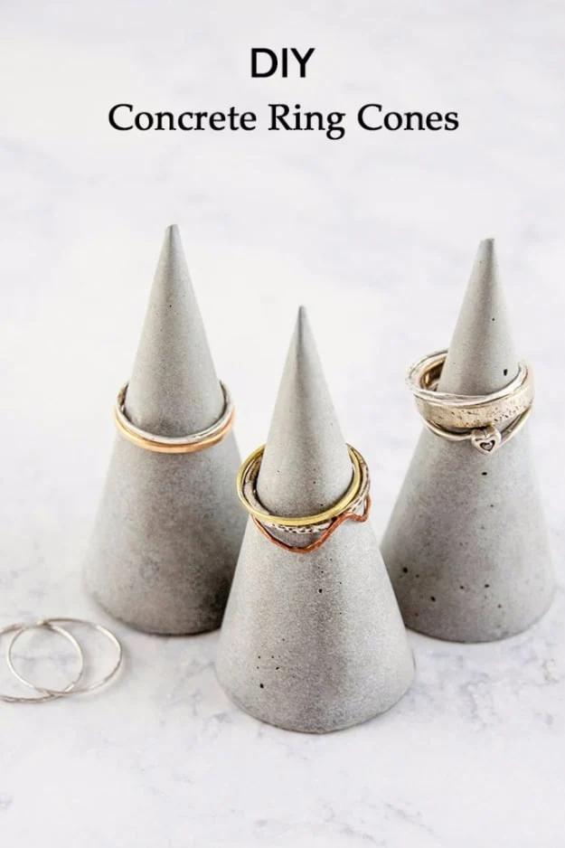 Three grey concrete cones with gold dipped tips on a marble surface, one holding a thin gold stacking ring