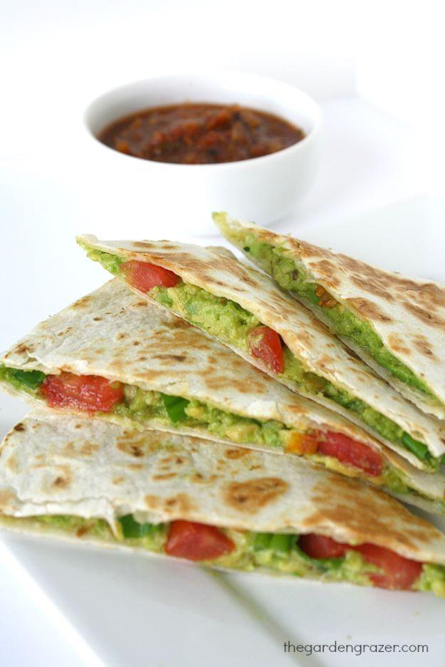 Avocado quesadillas cut into wedges on a white plate showing green avocado and tomato filling, salsa behind