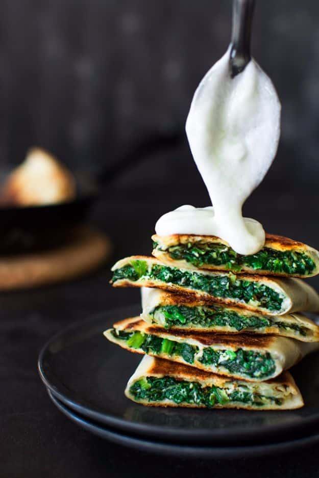 Stacked spanakopita quesadilla wedges packed with dark spinach as sour cream is spooned over the top
