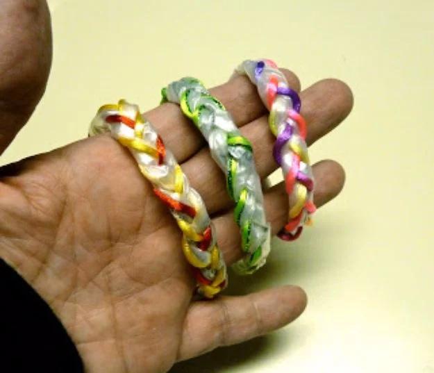 Three braided bracelets made from clear plastic bags with yellow, green and pink satin cord, held in an open palm