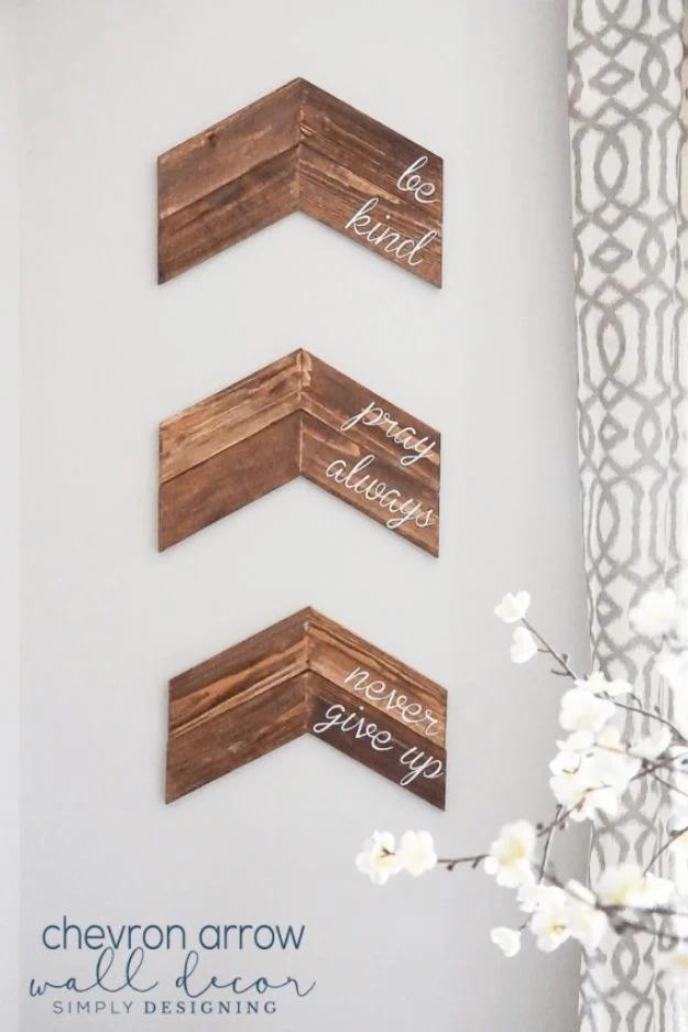 A painted wood chevron arrow with a name lettered across it hangs on a pale wall above a wooden bench