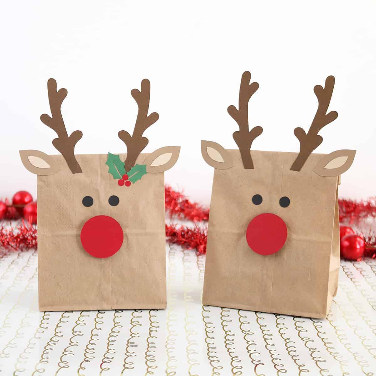 Two brown paper lunch bags turned into reindeer gift bags with cardstock antlers, ears and big red noses
