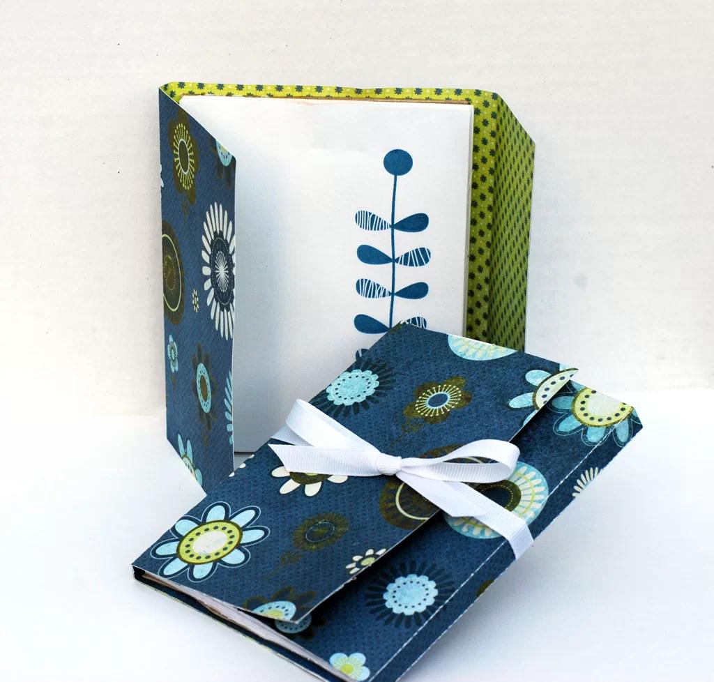 Handmade paper notepad with a navy floral cardstock cover tied with white ribbon, standing open on a white surface