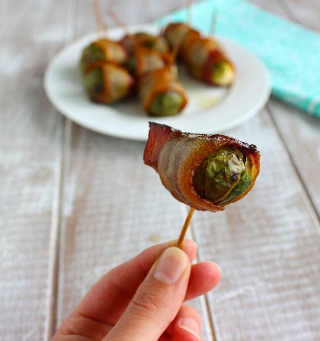 Bacon wrapped brussels sprouts pinned on toothpicks, one held to the camera with a white plate behind it