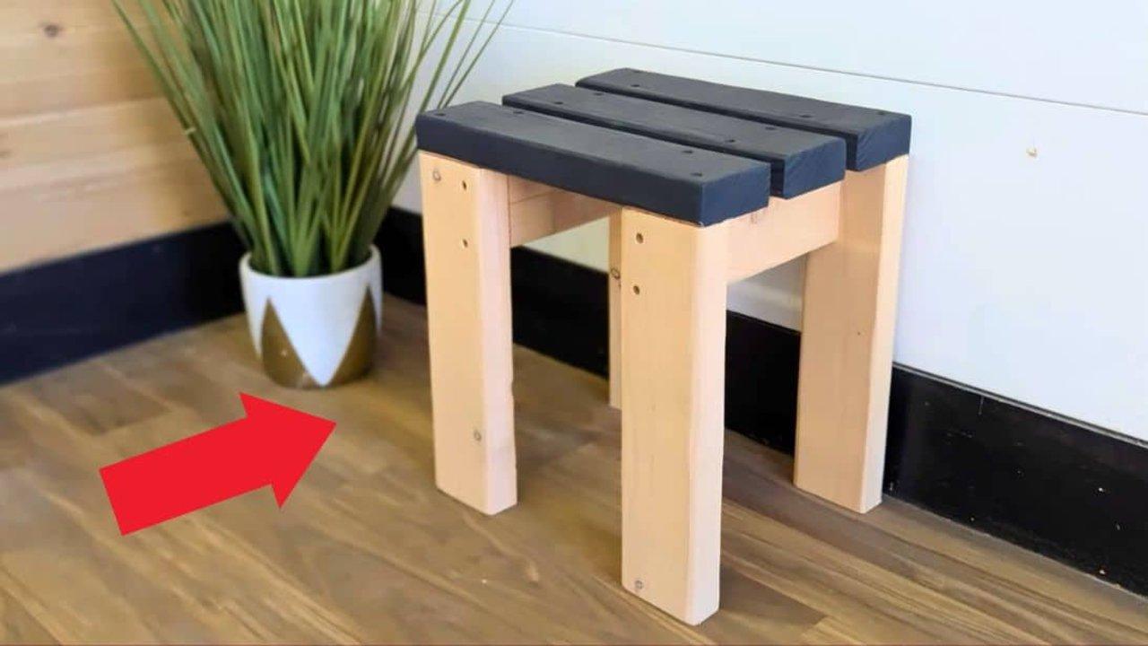 DIY stool built from a single 2x4 with a slatted top painted dark gray on natural pine legs beside a potted plant