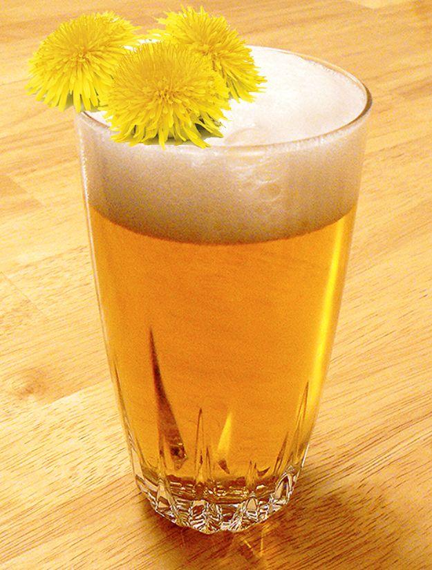 Dandelion beer in a tall glass, pale gold and lightly hazy, beside a handful of fresh dandelion heads