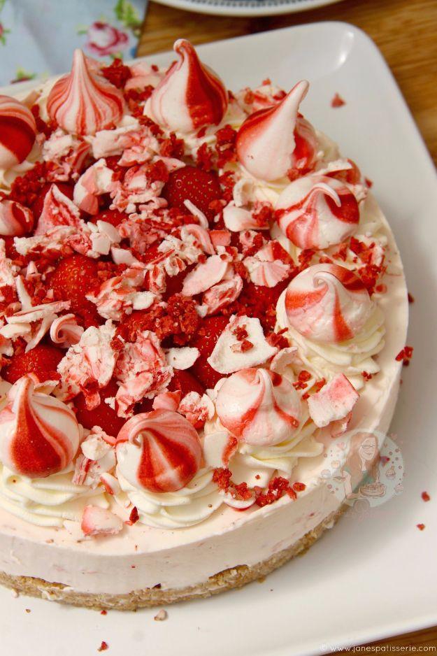 No bake Eton mess cheesecake covered in pink and white meringue pieces and strawberries on a white platter