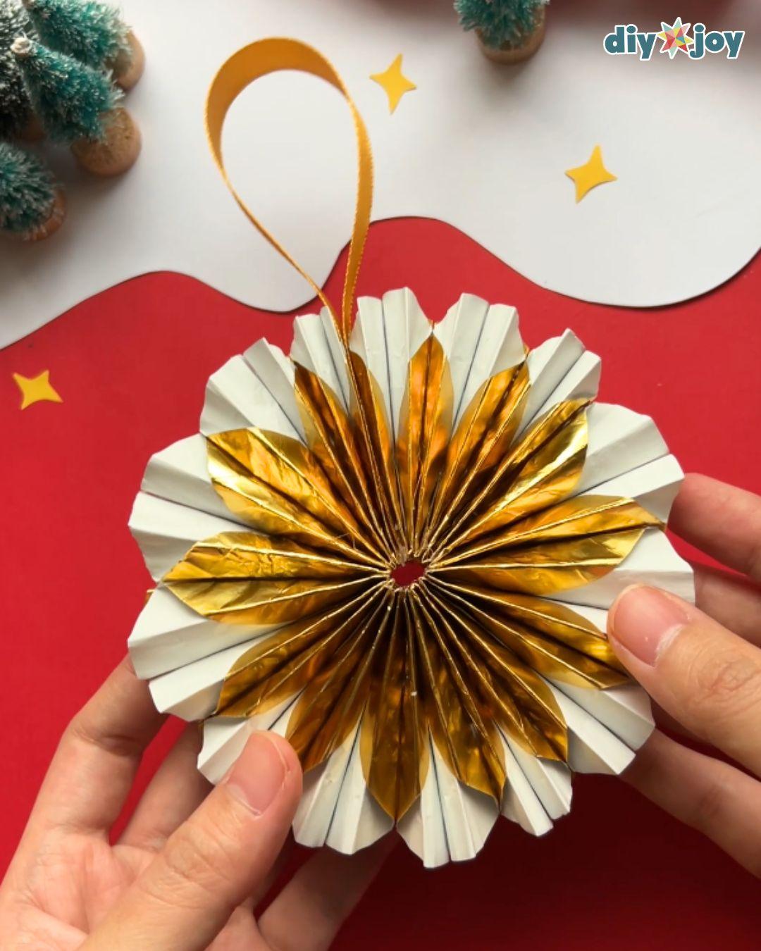 DIY Christmas ornament finished as a round gold and white paper fan with a ribbon loop, held in two hands