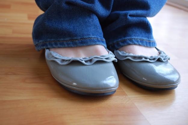 Pair of gray patent ballet flats trimmed with a gathered gray zipper ruffle around the opening, worn with jeans