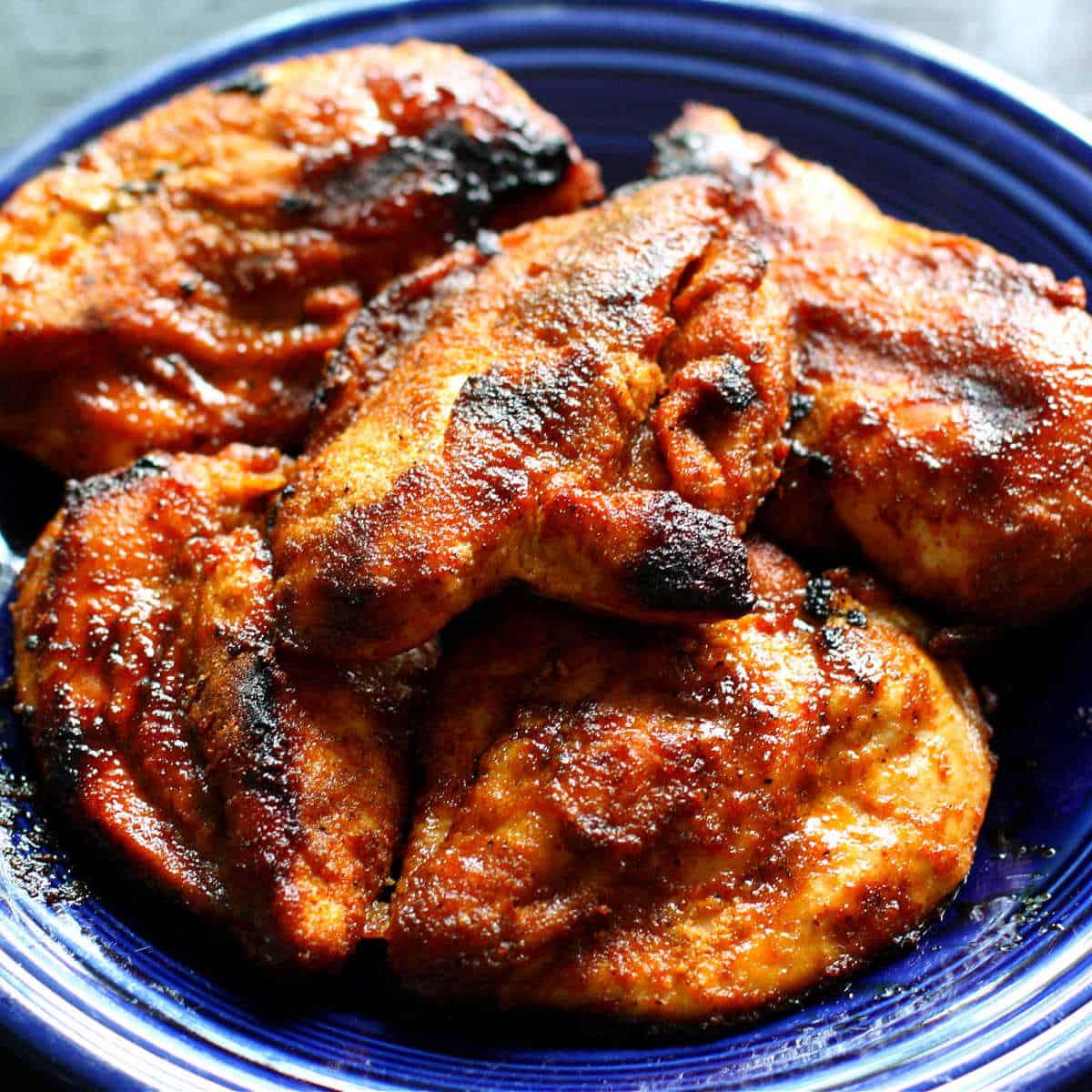 Grilled chicken breasts coated in a sweet and smoky homemade barbecue spice rub piled on a cobalt blue dinner plate