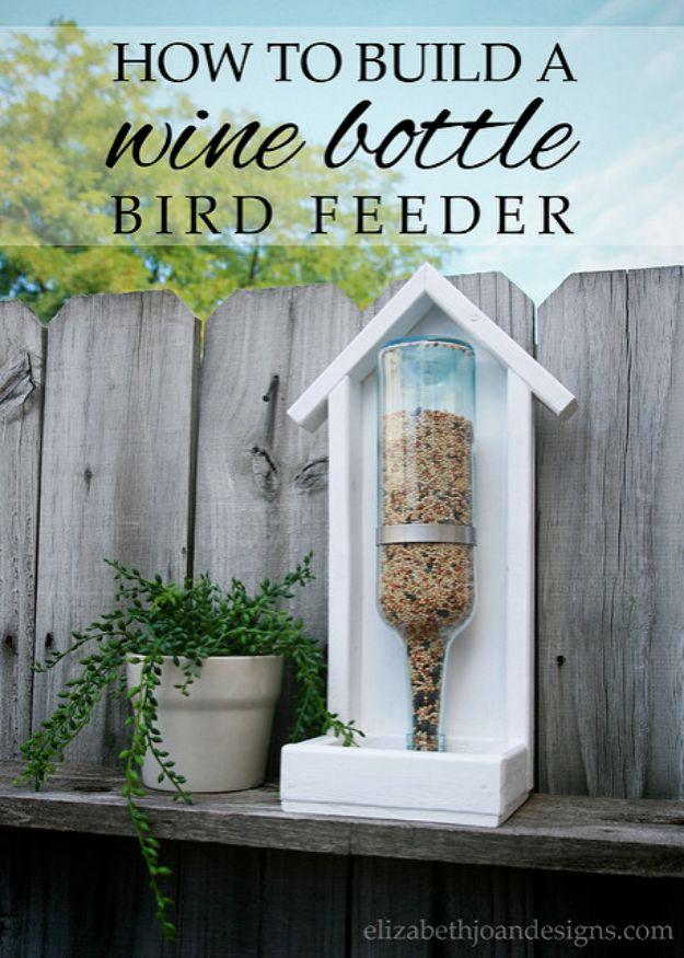 DIY wine bottle bird feeder in a white painted wood frame on a weathered fence, seed filled bottle inverted inside