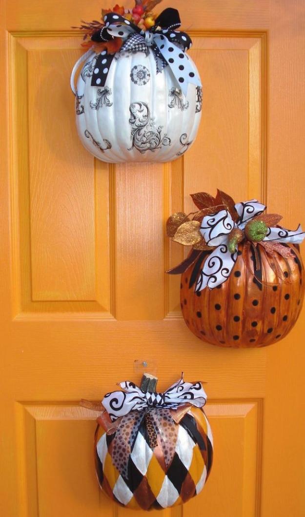 Three decorated half pumpkins hung down an orange front door, each with a black and white ribbon bow