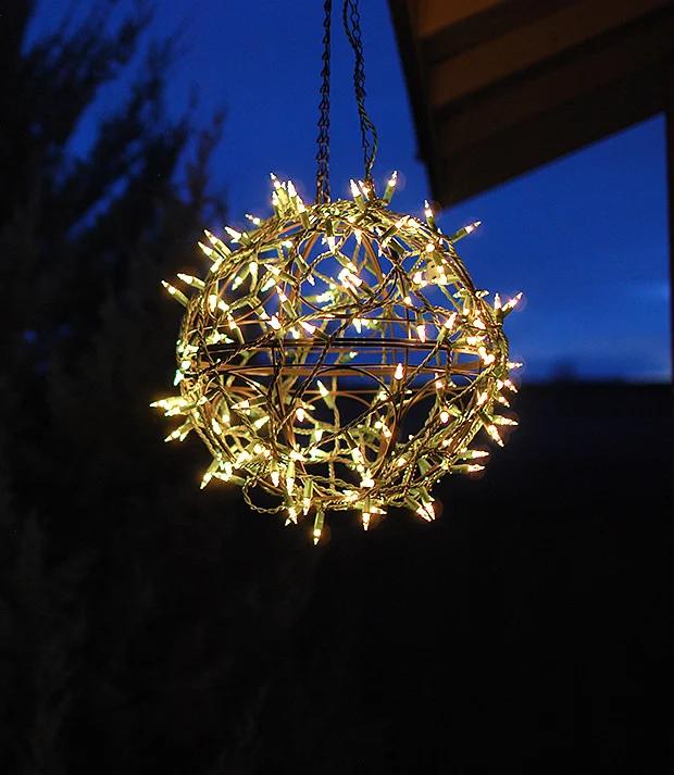 Glowing sphere made from two wire garden baskets wrapped in clear mini lights hanging from a porch beam