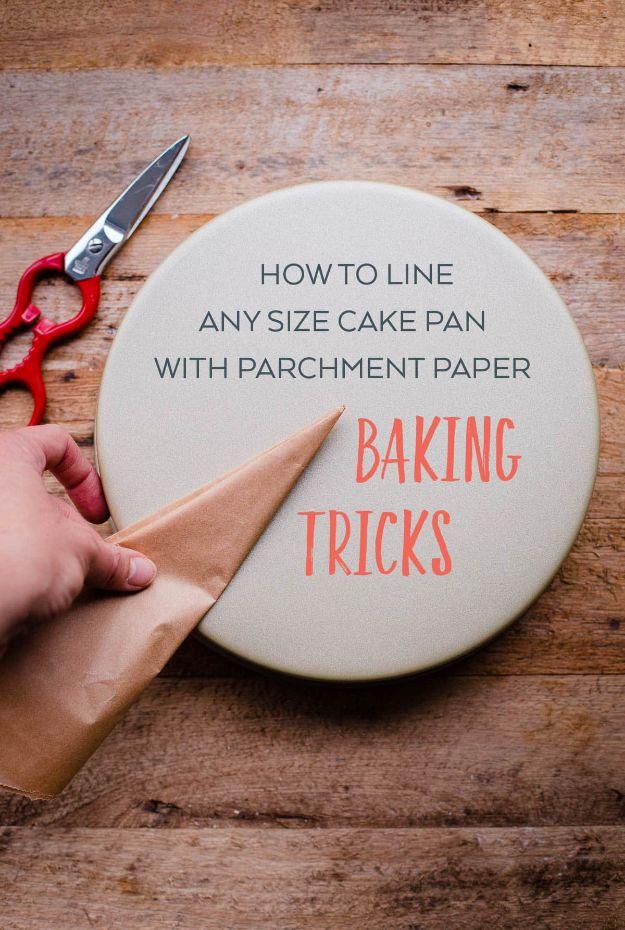 Hand folding a sheet of parchment paper into a triangle beside a round cake pan and red scissors on a wood table