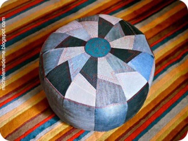 Round denim patchwork pouf pieced from twelve light and dark jean wedges with a teal center circle on a striped rug
